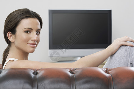 沙发上年轻女性在平板屏幕电视肖像前男人客厅微笑女士成人活动黑发摄影真皮成年图片