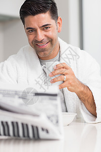 在厨房看报纸时 微笑的男人带着咖啡杯图片
