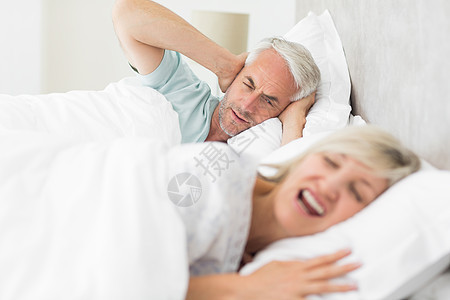 男人耳罩 而女人在床上喊叫家庭生活羽绒被睡眠愤怒休息夫妻觉醒男性床单女性图片