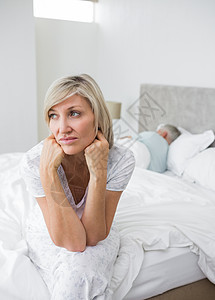 与背景男子一起坐在床上的十几岁的成年妇女睡眠夫妻思维家庭生活忧郁悲哀卧室女性愁云悲伤图片