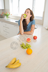 妇女在厨房柜台上吃有水果的苹果图片