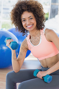 微笑的年轻女子在健身房用哑铃锻炼健身室培训师肌肉卷发运动活动护理重量运动服讲师图片
