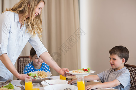 母亲在餐桌上为儿子做意面图片