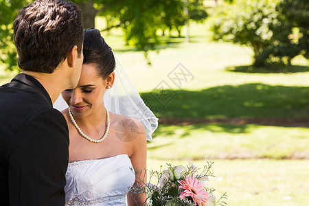 Groom在公园亲吻他的漂亮新娘团结女士男人联盟庆典婚纱已婚男性婚礼面纱图片