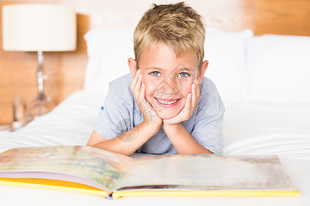 躺在床上看故事书的金发男孩微笑图片