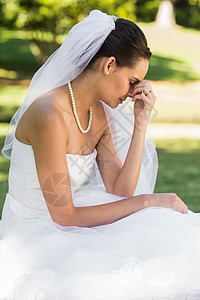 坐在公园的美丽忧郁新娘珍珠婚礼裙子项链愁云悲伤草地新人婚姻女士图片