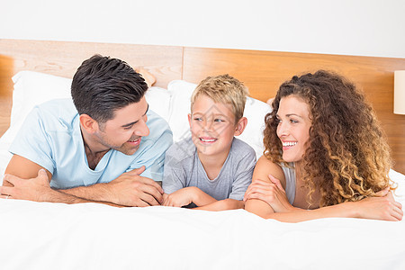 幸福的年轻家庭躺在床上互相看着对方图片