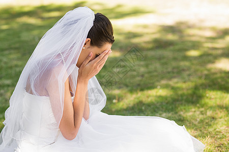 坐在公园的美丽忧郁新娘草地婚纱愁云婚姻婚礼新人女性女士面纱悲伤图片