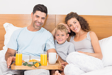 快乐的年轻家庭在床上吃早餐头发浅色孩子男生金发女郎儿子父亲羽绒被金发微笑图片