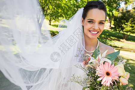 带着花束在公园中微笑的年轻美丽新娘已婚草地面纱婚礼女性快乐婚姻婚纱裙子新人图片