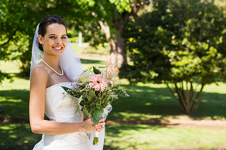 带着花束在公园中微笑的年轻美丽新娘女士婚纱草地婚姻裙子新人女性面纱已婚快乐图片