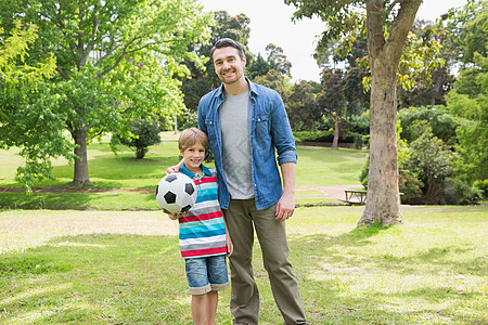 父亲和儿子在公园玩球的肖像运动俏皮足球草地团结闲暇童年花园男人树木图片