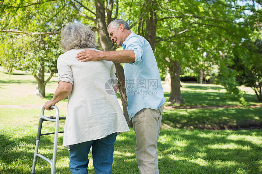 成年男子在公园用步行器协助妇女残障退休病人成人女士身体女性草地照顾者人士图片