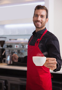 微笑的年轻咖啡师拿着茶壶和咖啡图片
