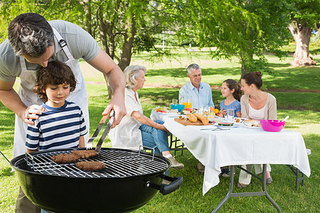 父亲和儿子在烧烤炉上 家人一起在公园吃午饭准备孙女孙子炙烤女孩父母妈妈家庭午餐男生图片