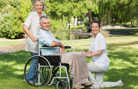成年男子坐在公园轮轮椅上的妇女病人草地辅助男人机动性成人女性树木父亲功能图片