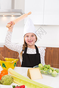 女厨师 用滚动的金球做反顶式滑稽手势孩子们孩子戏服滚筒食物桌子厨房微笑蓝色金发图片