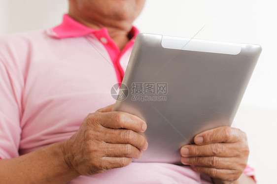 高级男子使用数字平板电脑商务沙发男人房子技术电子老年人白色软垫学习图片