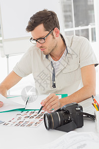 集中男性艺术家与照片坐在桌上的桌子上设计师女士专注职业公司便服摄影办公室机构编辑图片