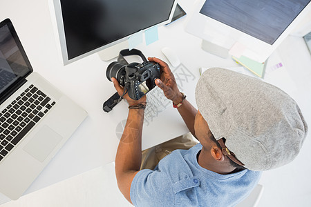 照片编辑在办公室看数码相机的照片编辑专注男人黑色男性桌子电脑平顶公司摄影电子图片