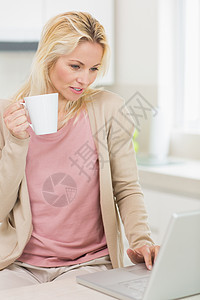 在厨房用笔记本电脑装咖啡杯的漂亮女人杯子技术饮料闲暇金发女郎家庭生活女士房子女性咖啡图片