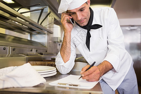 在厨房使用手机时在剪贴板上写作男性职业笔记呼唤专注白人厨师电话沟通工作图片