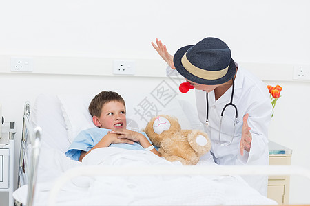 医生在医院床上招待生病的男孩毛绒玩具熊监视保健安慰病人女性制服服务小丑图片