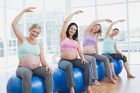 坐在锻炼球上伸展手臂的孕妇图片