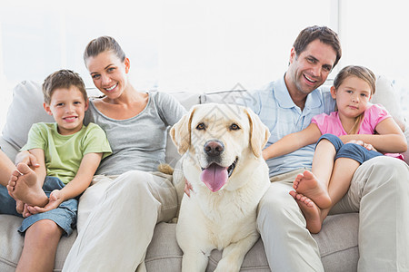 幸福的一家人和宠物拉布拉多人一起坐在沙发上图片