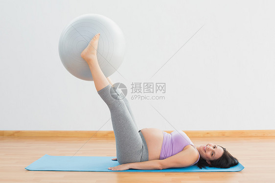 微笑的孕妇用双腿举起运动球图片