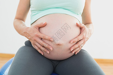 坐在锻炼球上的孕妇抱着她的肚子;图片