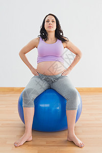 坐在蓝色运动舞会上的怀孕妇女健身室腹部健身房运动服身体竞技女士护理女性待产背景图片