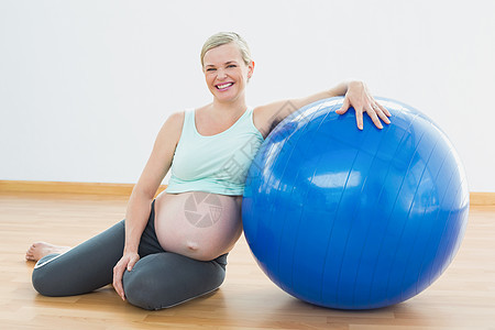 坐在健身球旁边的孕妇在镜头上微笑着微笑怀孕男人运动服腹部健身房瑜伽孕妇装健身室倾斜地面图片