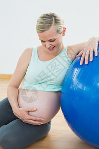 微笑的孕妇靠着运动球抱着她的肚子向她笑图片