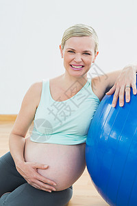快乐的孕妇靠在运动球上抱着肚子 紧紧抓住她的肚子图片