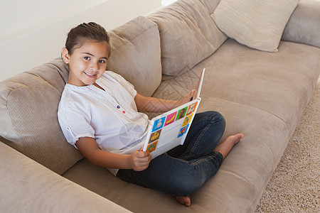 一个女孩在沙发上读故事书的侧面肖像图片