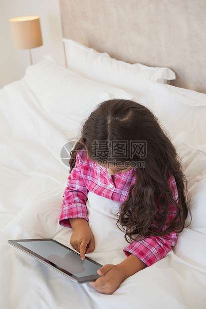 年轻女孩在床上使用数字平板电脑头发触摸屏闲暇公寓长发羽绒被滚动枕头童年药片图片