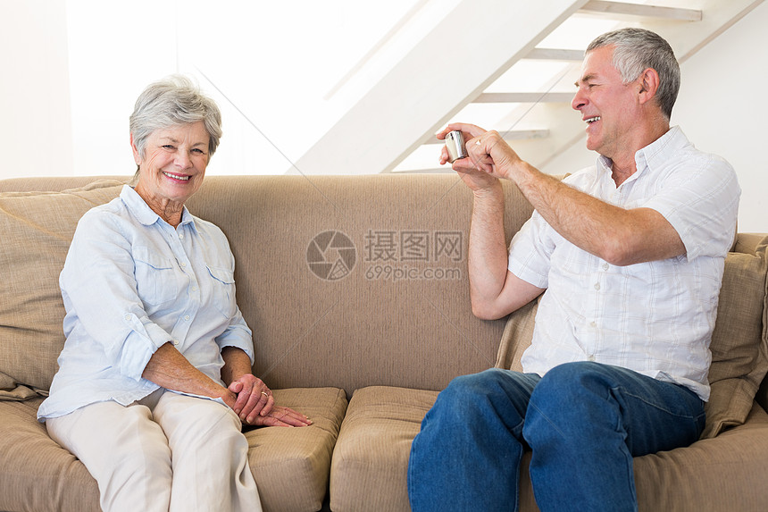 退休男子在沙发上拍他搭档的照片头发男人女士家庭闲暇长椅拍照客厅男性公寓图片