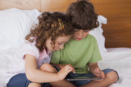 在床上使用数字平板电脑的男女儿童图片