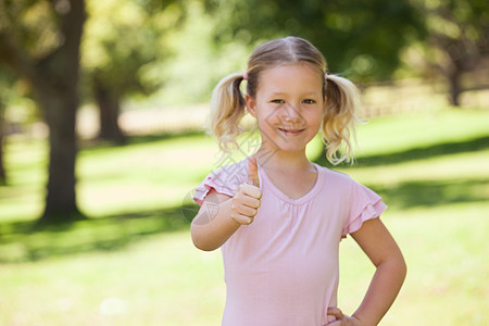 微笑的女孩在公园里挥舞着拇指沟通闲暇童年双手金发女郎手势头发浅色绿色绿地图片
