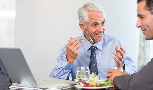两名商务人士在吃饭时使用笔记本电脑桌子沙拉技术果汁合作伙伴食物橙汁合伙男性图片