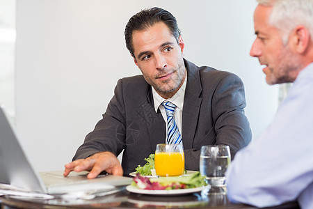 商务人士在吃饭时使用笔记本电脑技术男人桌子合作套装玻璃橙汁伙伴商务男性图片