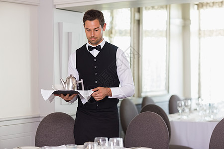 手持托盘和餐桌的英俊服务员图片