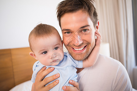 父亲和儿子坐在床上 在蓝色的婴儿园里新生活住所婴儿男性男生服装幸福微笑家庭公寓图片