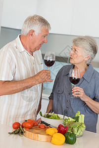 准备沙拉和喝红酒的老夫妇微笑闲暇素食者感情沙拉头发健康饮食女士房子亲密感切菜板图片