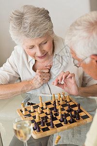 玩象棋和喝白酒的老夫妇微笑棋盘快乐酒精男性住所酒杯老年退休家庭厨房图片