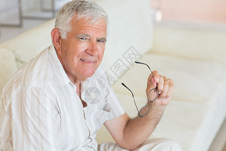 坐在沙发上拿着眼镜的快乐高官男性公寓老年成人房子客厅头发退休男人家庭图片