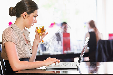 在笔记本电脑上工作时持有葡萄酒杯的有吸引力的商业妇女图片