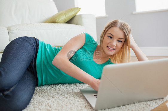 快乐的女士躺在地板上看着笔记本电脑屏幕图片