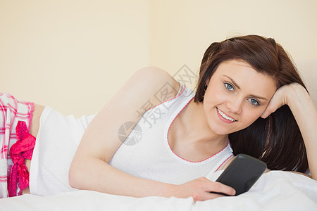 微笑的女孩用手机在床上看照相机 躺在床上图片